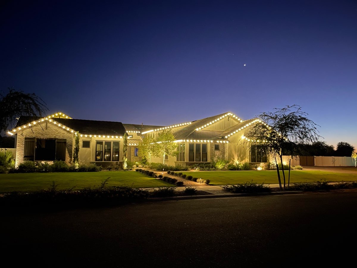 A home lit with warm white roofline lights at dusk
