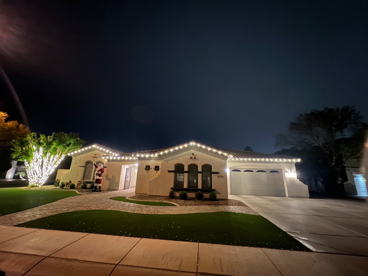 A home with warm white roofline lights and a lit tree